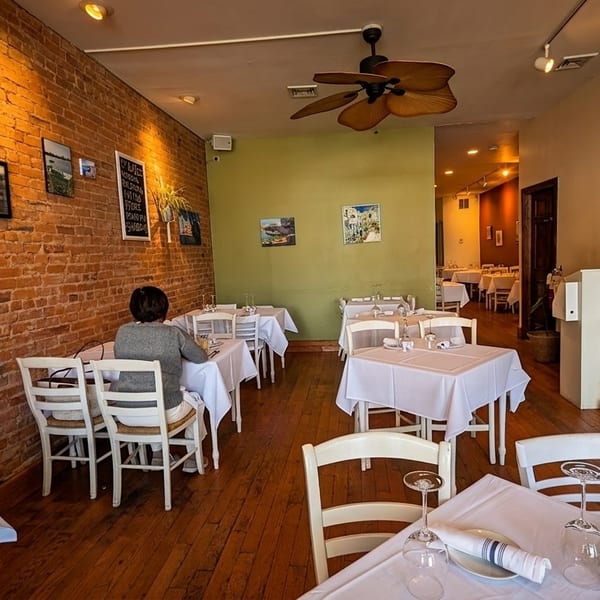 A restaurant dining room with brick walls, white-clothed tables, and a person seated at a table.