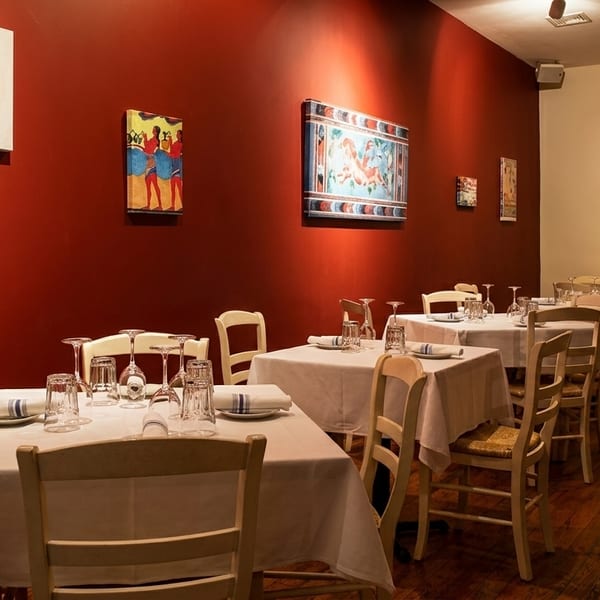 Restaurant interior with red walls, white tablecloths, set tables, and colorful artwork.