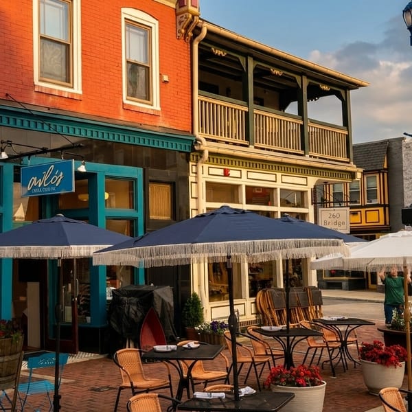 A vibrant street scene with outdoor dining tables and umbrellas in front of brick buildings.