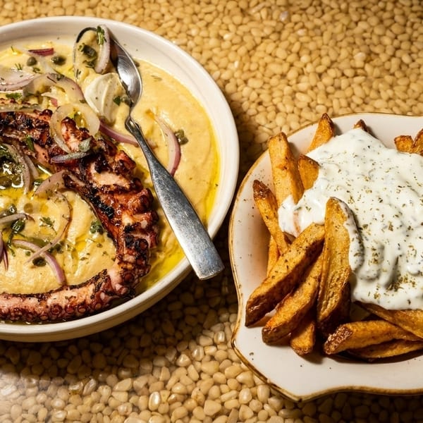 Grilled octopus with red onions and capers on a bed of hummus, next to a plate of french fries with tzatziki.